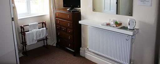 An image of a bedroom with a window, radiator, chest of drawers, towel stand and mirror.