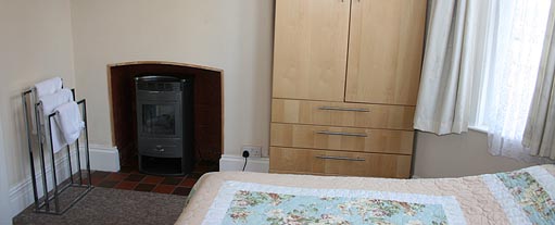 An image of a bedroom with a built in stove with a towel stand next to it, there is also a wardrobe.