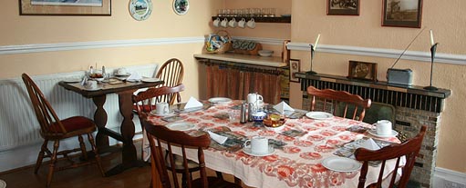 An image of a traditional breakfast room with tables laid out with table cloths, cutlery and crockery.