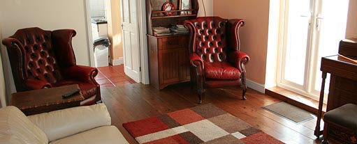 An image of a cosy sitting room containing two red leather buttoned wing chairs and a cream sofa, there is a dresser in the background.